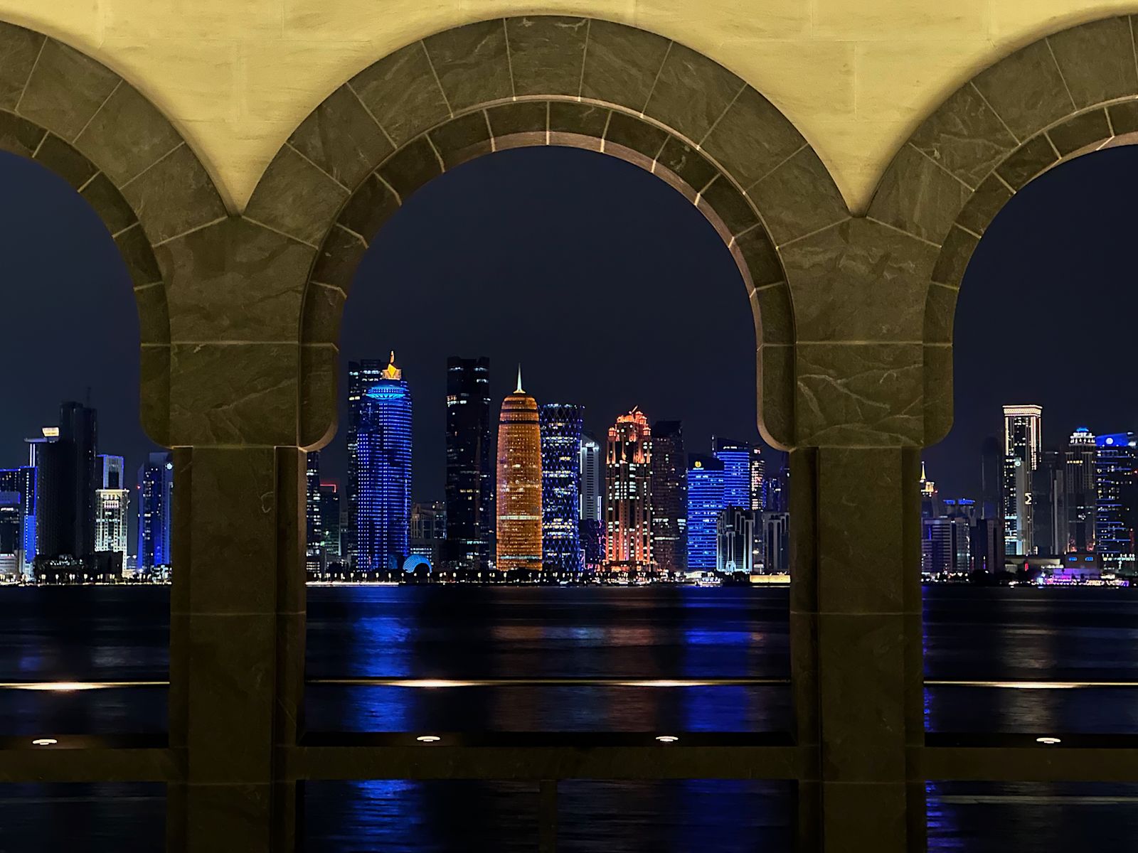 Doha skyline at night, framed by stone arches